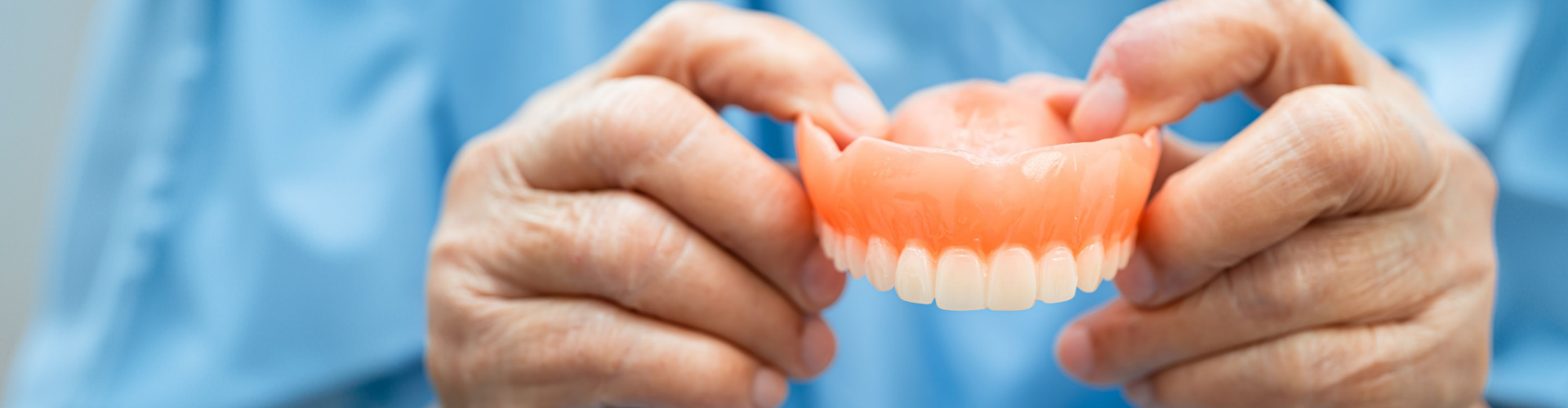 Close-up of hands holding a full upper denture, showcasing a natural-looking removable prosthetic designed to replace missing teeth and restore a complete smile.